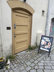 Foto av en gul dør i en gulhvit murbygning. En skiltbukk med teksten "Hexagon" står ved siden av døra